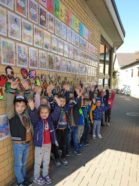 Bild vergrößern: Mehrere Kinder vor einer Wand mit Bildern und Hand-Abdrcken.