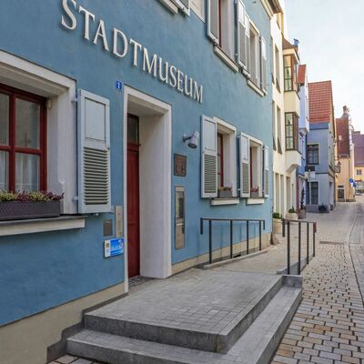 Seitliche Aufnahme von der blauen Fassade des Stadtmuseums. Über der hölzernen Eingangstür hängt in silbernen Großbuchstaben der Schriftzug "Stadtmuseum"