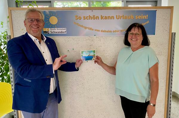 Bild vergrößern: Das Bild zeigt zwei Personen vor einer Stellwand. Sie werben für die Post-Kartenaktion der Stadt Schwandorf.