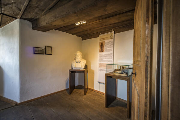 Im kleinen Zimmer steht in der Ecke auf einem kleinen Holztisch die weiße Büste von Konrad Max Kunz. Der Boden ist aus Holzdielen, genauso die Decke. 