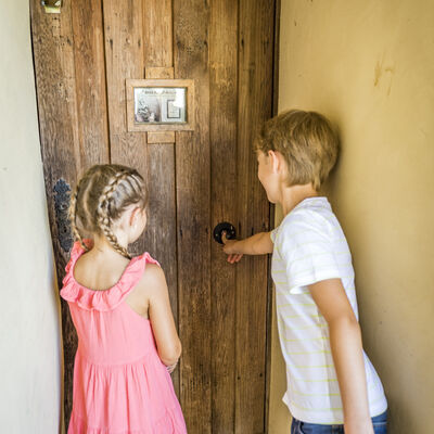 Vor der Holztr stehen zwei Kinder, ein Mdchen und ein Bub, und horchen der Aufnahme des Kndelliedes zu. 