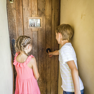 Vor der Holztür stehen zwei Kinder, ein Mädchen und ein Bub, und horchen der Aufnahme des Knödelliedes zu. 