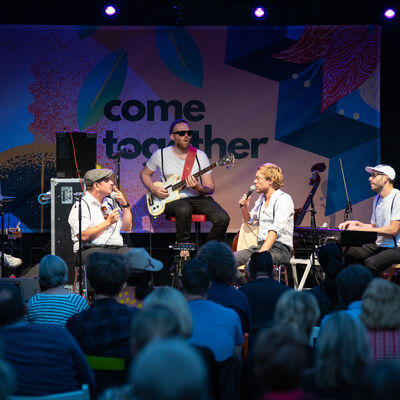 Band auf der Bühne. Im Vordergrund verschwommenes Publikum.