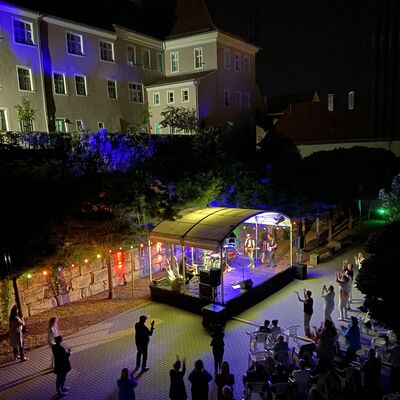 Bunt beleuchtete Bühne bei Nacht im Spitalgarten. Um die Bühne herum stehen mehrere Personen und klatschen.