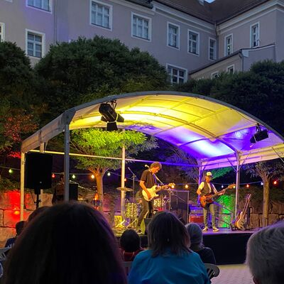 Blick aus dem Publikum zur Band auf der bunt beleuchteten Bühne im Spitalgarten bei Dämmerung.
