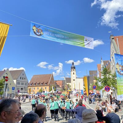 Eine Gruppe in gleichen türkisen Shirts geht als Teil eines Festzugs den sonnigen Marktplatz hinauf. Mehrere Zuschauer beobachten sie.