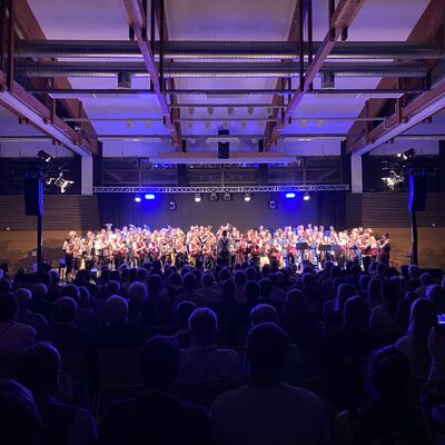 Ein großer Chor singt auf einer beleuchteten Bühne. Davor sitzt das Publikum.