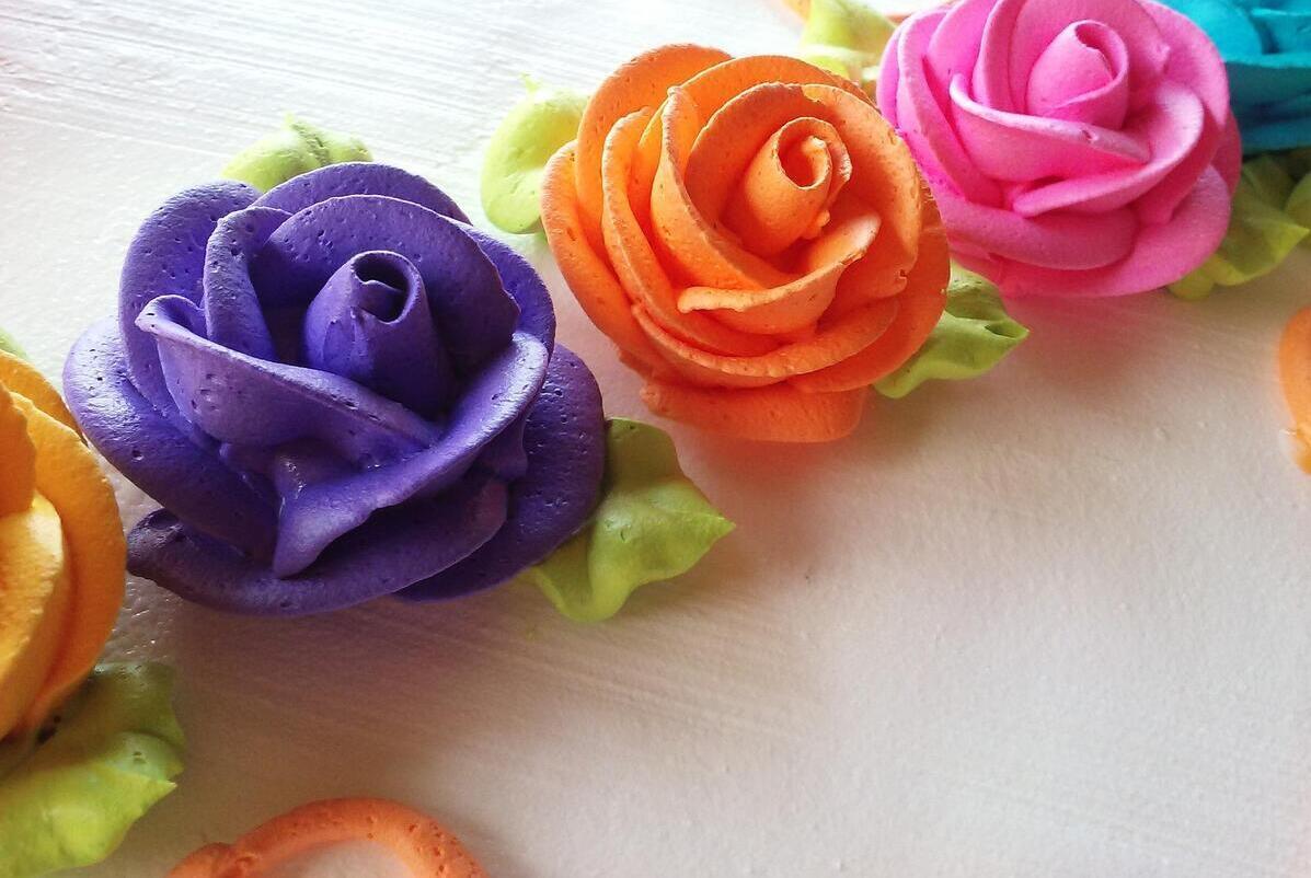 Eine lila, eine orange und eine pinke Blume aus Buttercreme gespritzt