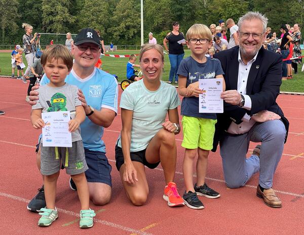 DAs Bild zeigt drei Erwachsene und zwei Kinder. Die Kinder haben eine Urkunde fr sportliche Leistungen in der Hand.