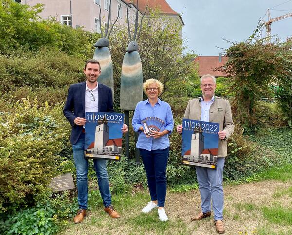 Das Bild zeigt zwei Mnner und eine Frau vor einer Skulptur im Grnen.