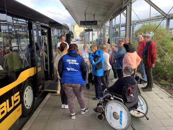 Bild vergrößern: Das Bild zeigt mehrere Menschen, die mit Rollstuhl und Rollatoren eine Probefahrt mit einem Bus machen.