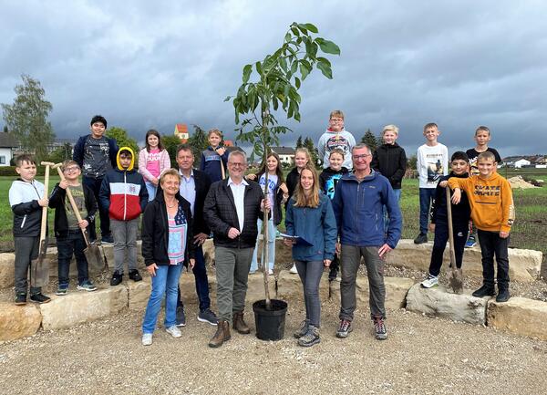 Bild vergrößern: Das Bild zeigt mehrere Personen, die einen Baum pflanzen.