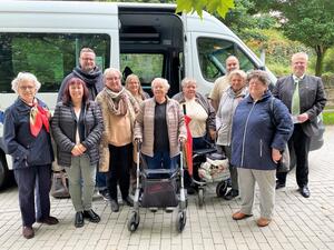 Bild vergrößern: Das Bild zeigt mehrere Personen vor einem kleinen Transportbus mit 20 Sitzpltzen.