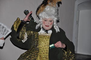 Bild vergr&ouml;&szlig;ern: Die Schauspielerin tr&auml;gt ein barockes Kleid in den Farben Schwarz und Gold. Auch auf der wei&szlig;haarigen Per&uuml;cke finden sich diese Farben in ihrem Federschmuck wieder.