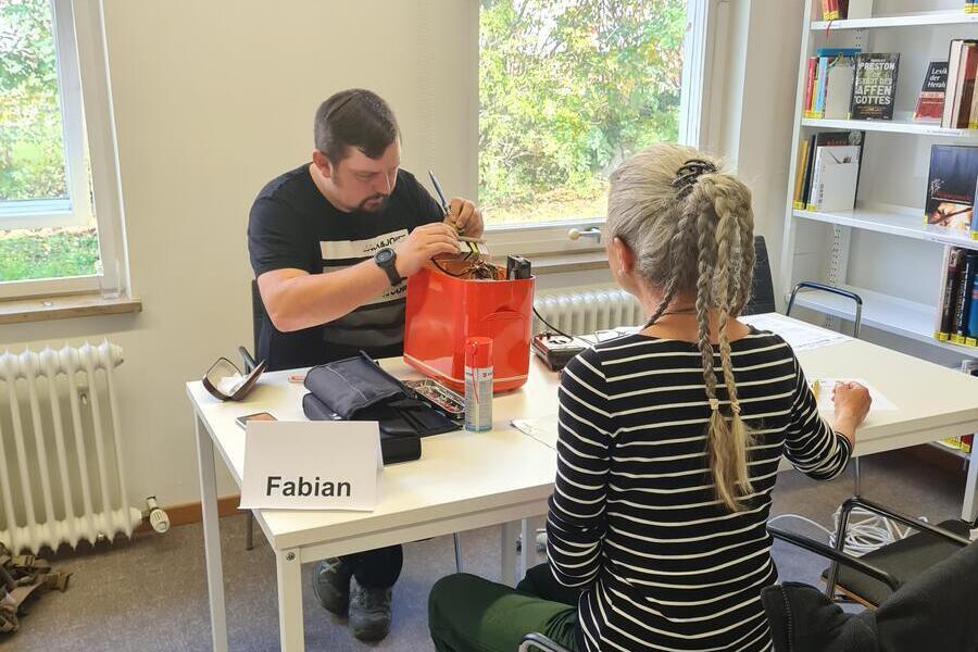 Zwei Menschen sitzen an einen Tisch und reparieren ein Gert