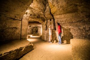 Bild vergrößern: Zwei Besucher sehen sich im gut beleuchteten Felsenkeller eine Spalte in der Wand an.