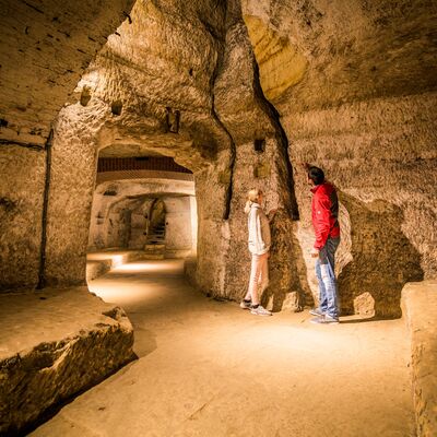 Zwei Besucher sehen sich im gut beleuchteten Felsenkeller eine Spalte in der Wand an.