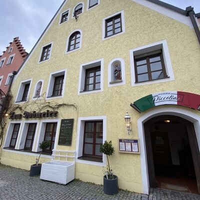 Bild vergrößern: Foto vom Gebude der Pizzeria Piccolino. Die Fassade ist gelb mit braunen Fenstern und ber der Eingangstr hngt ein Schild in den Farben der italienischen Flagge mit dem Namen der Pizzeria.