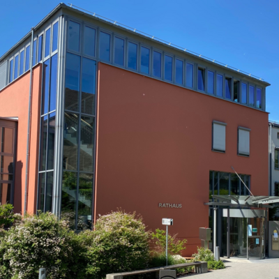 Foto vom Eingang des Rathauses. Die Fassade besteht zum Teil aus Glas und ist rot gestrichen.