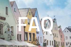 Foto der bunten Häuser am Schwandorfer Marktplatz. Im Vordergrund steht in großen, weißen Buchstaben "FAQ"