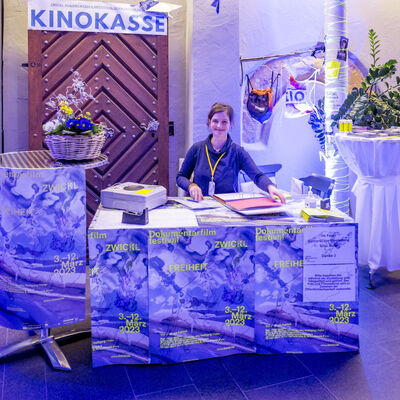 Eine Frau sitzt hinter der Kinokasse in der Spitalkirche. Der Kassentisch ist mit bunten Festivalplakaten beklebt.