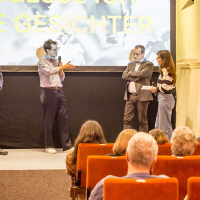 Die drei Gewinner des Bayerischen Dokumentarfilmpreises ZETT stehen auf der Bühne und sind im Gespräch mit der Moderatorin.