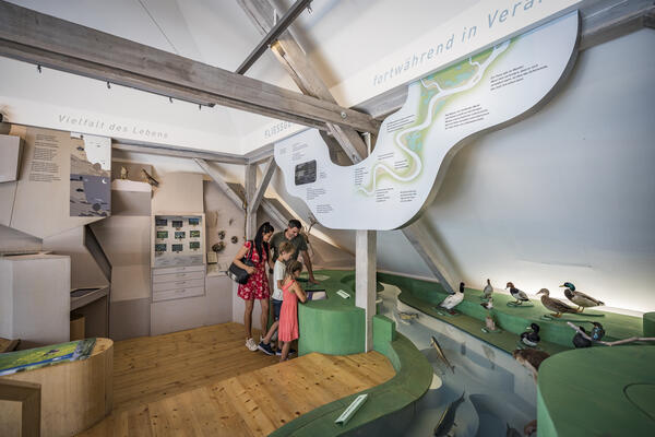 Bild vergrößern: Eine Frau steht mit zwei Kindern im NaturInfoZentrum des Stadtmuseums und betrachtet eine Infotafel