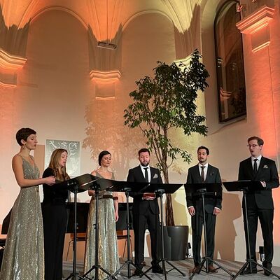 Die sechs Musikerinnen und Musiker des Vokalensembles StimmGold stehen festlich gekleidet hinter ihren Notenständern auf der Bühne.