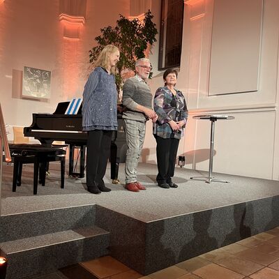 Der Künstler Peter Nüesch steht zwischen den beiden Pianistinnen Eva Herrmann und Inna Schur auf der Bühne der Spitalkirche.