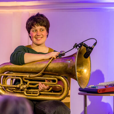 Die Musikerin Theresa Loibl sitzt mit ihrer Tuba auf dem Schoß auf der Bühne.
