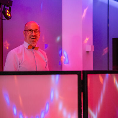 Foto des DJs. Die Beleuchtung ist rosa und blau.