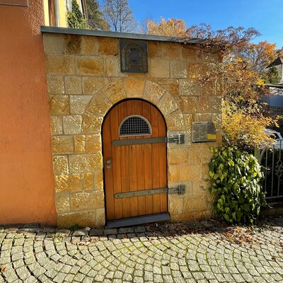 Bild vergrößern: Foto vom Eingang zum Felsenkeller-Labyrinth. Zu sehen ist eine hlzerne Tr, die in eine Mauer mit groen, sandfarbenen Steinen eingelassen ist.