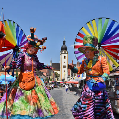 Bild vergrößern: Zwei als bunte Gaukler verkleidete Stelzenkünstler auf dem Schwandorfer Marktplatz.