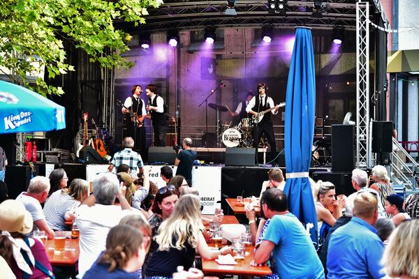 Bild vergr&ouml;&szlig;ern: Die Beatles-Coverband spielt auf der B&uuml;hne am Adolf-Kolping-Platz. Davor sitzt das Publikum an Biertischen.