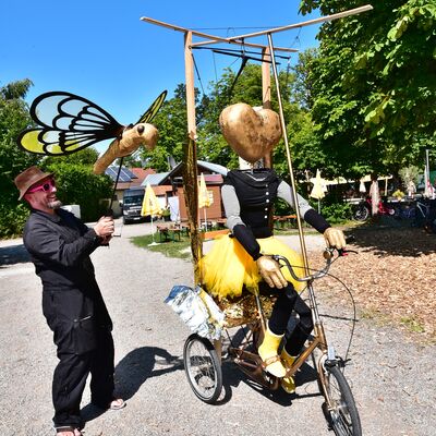 Bild vergrößern: Das Schwandorfer Marionettentheater ist mit einer übergroßen Marionette mit goldenem Herzkopf auf einem Fahrrad und einer einer großen goldenen Fliege auf dem Bürgerfest unterwegs.
