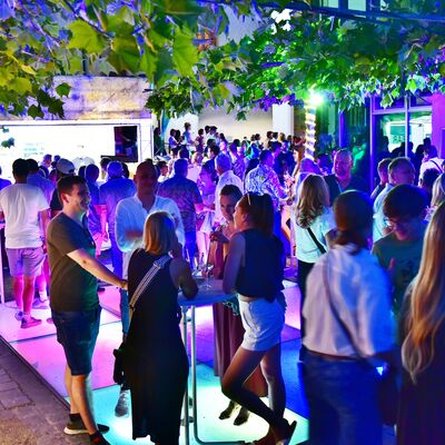 Bild vergrößern: Besucher:innen des Bürgerfests stehen an Stehtischen auf dem bunt beleuchteten gläsernen Tanzboden.