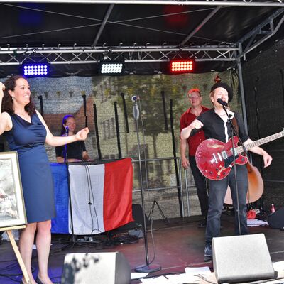 Bild vergrößern: Vier Musiker der französischen Chanson-Band "French Kiss" performen auf der Bühne. Im Hintergrund ist eine französische Flagge zu sehen.