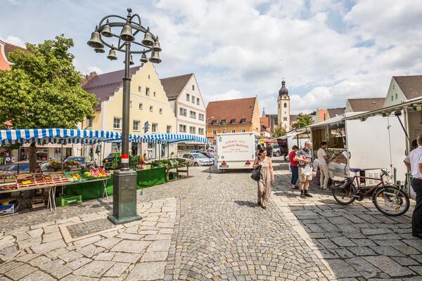 Bild vergrößern: Schwandorfer Markt an einem sonnigen Tag auf dem Marktplatz. Es sind Personen, die einkaufen und im Hintergrund die Jakobskirche zu sehen.