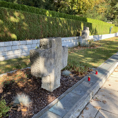 Bild vergrößern: Ein greres Kreuz aus Stein steht fr die Opfer des Kriegs am Friedhof, davor stehen noch zwei kleine rote Grablichter.