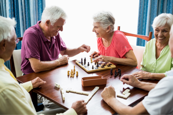 Senioren sitzen lachend am Tisch und spielen Schach