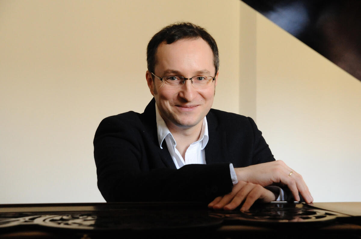 Porträtaufnahme des Pianisten Christian Seibert. Er sitzt an einem Klavier und lächelt in die Kamera.