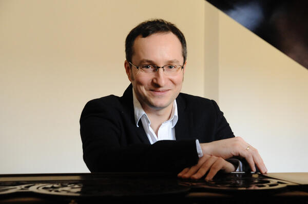 Portrtaufnahme des Pianisten Christian Seibert. Er sitzt an einem Klavier und lchelt in die Kamera. 