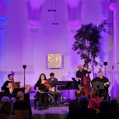 Die Musikerinnen und Musiker des Quintetts Balkon Jazz Ballett sitzen auf der lila und blau ausgeleuchteten Bühne der Spitalkirche.