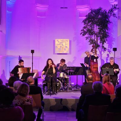Die Musikerinnen und Musiker des Quintetts Balkon Jazz Ballett sitzen auf der lila und blau ausgeleuchteten Bühne der Spitalkirche.