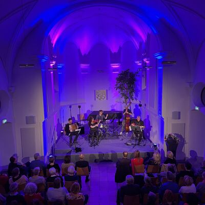 Die Musikerinnen und Musiker des Quintetts Balkon Jazz Ballett sitzen auf der lila und blau ausgeleuchteten Bühne der Spitalkirche.