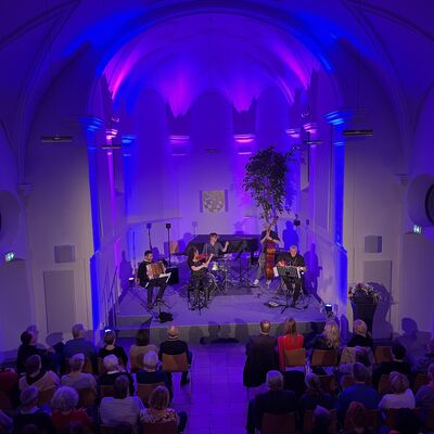 Die Musikerinnen und Musiker des Quintetts Balkon Jazz Ballett sitzen auf der lila und blau ausgeleuchteten Bhne der Spitalkirche.