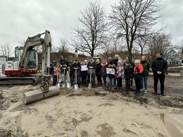 Mehrere Erwachsene und Kinder auf einer Baustelle mit Spaten in der Hand.