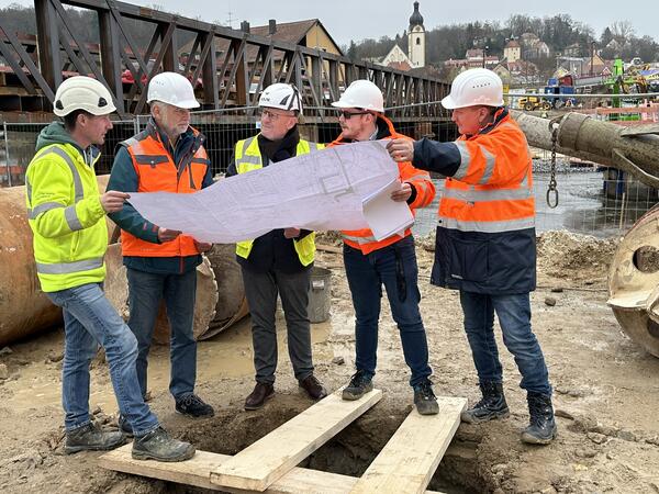 Mehrere Personen auf einer Baustelle. Sie schauen einen Bauplan an.