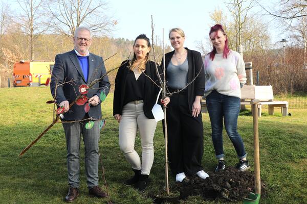 Ein Mann und drei Frauen pflanzen einen Apfelbaum.