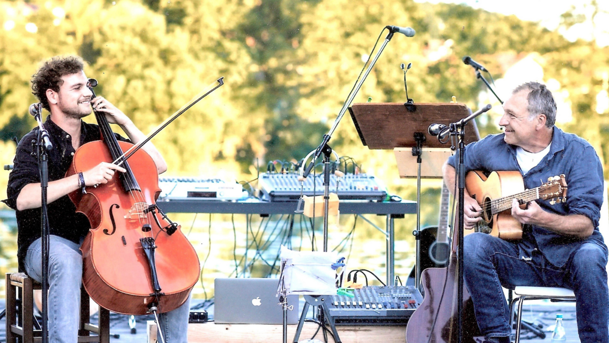 Das Duo "Father and Son" sitzt auf der Bühne. Yankee Meier spielt Gitarre, sein Sohn Christoph spielt Cello.